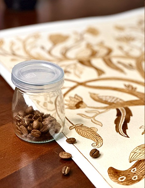 A jar of coffee beans resting on a patterned tablecloth, with loose beans scattered around it