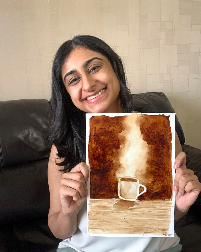 The artist behind Made with Beans, holding up a finished coffee painting